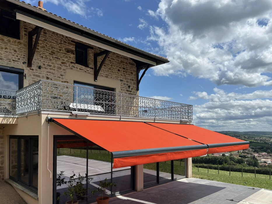Terrasse extérieure d'une maison en pierre avec store banne orange déployé