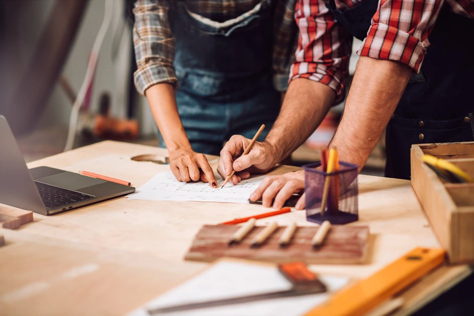 Artisan menuisier souriant dans son atelier de menuiserie, tenant une équerre en bois