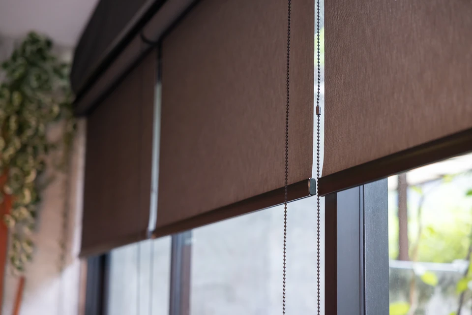 Intérieur moderne avec grandes baies vitrées, stores enrouleurs dégradé orange installés, ampoules suspendues style industriel, plantes vertes en pots sur rebord de fenêtre