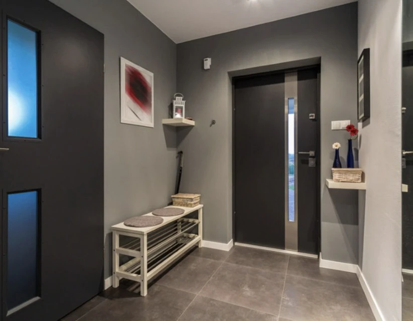 Façade extérieure d'une maison traditionnelle en pierre calcaire avec volets battants bordeaux, porte d'entrée vitrée assortie et véranda attenante