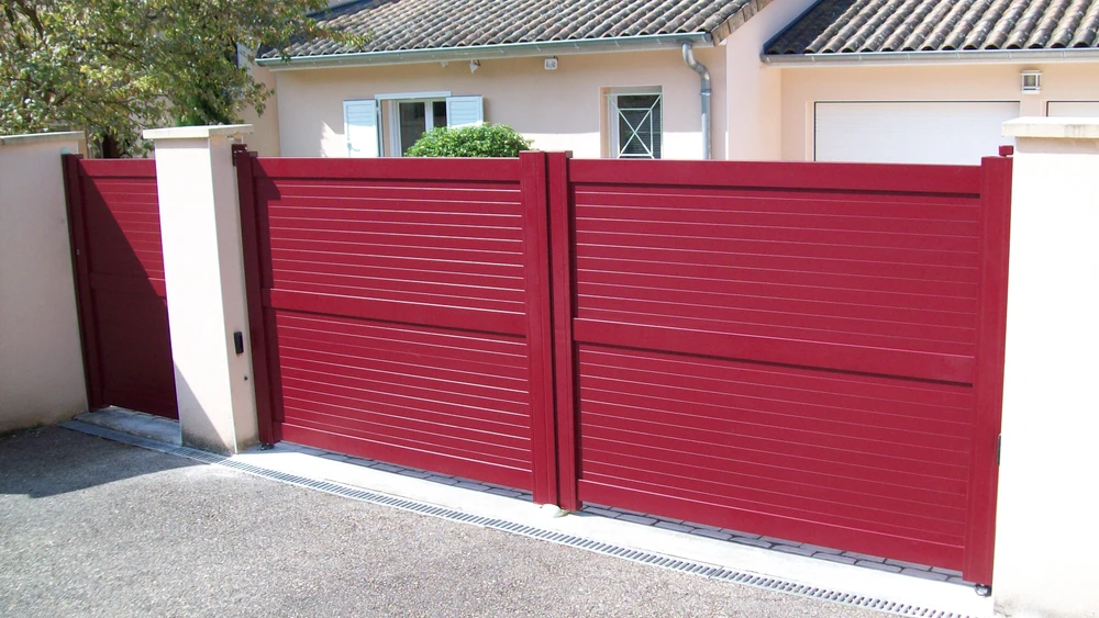 Portail métallique noir automatique ouvert sur route asphaltée, vignoble en arrière-plan