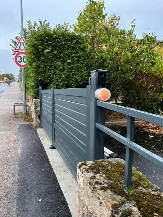 Portail métallique noir automatique ouvert sur route asphaltée, vignoble en arrière-plan
