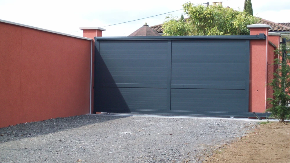 Portail métallique noir automatique ouvert sur route asphaltée, vignoble en arrière-plan