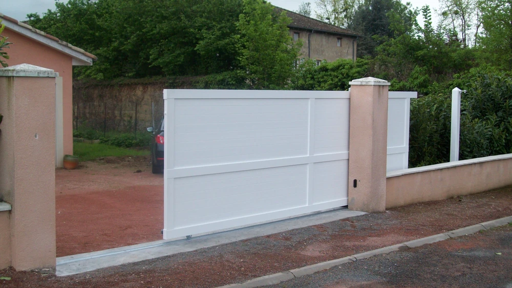 Portail métallique noir automatique ouvert sur route asphaltée, vignoble en arrière-plan
