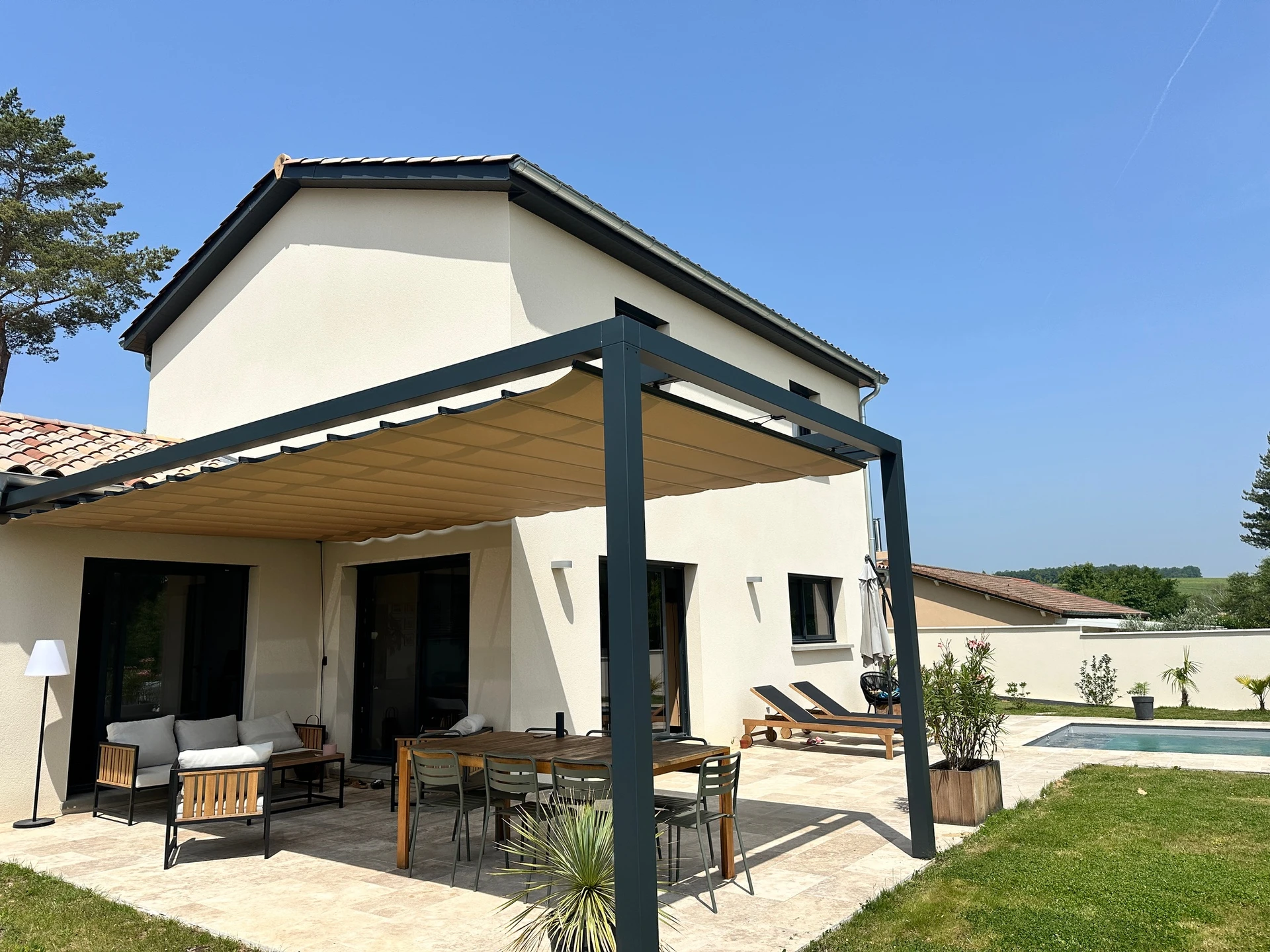 Terrasse couverte aménagée avec salon de jardin en résine tressée, coussins bleus, balancelle suspendue