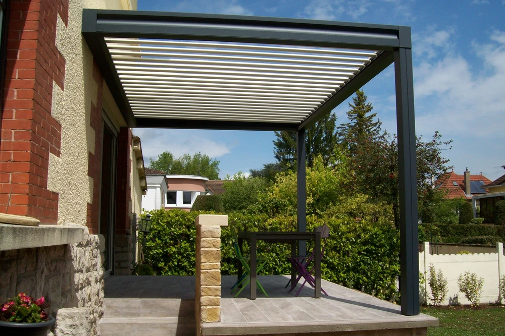Terrasse extérieure résidentielle avec pergola bioclimatique à lames orientables installée contre façade
